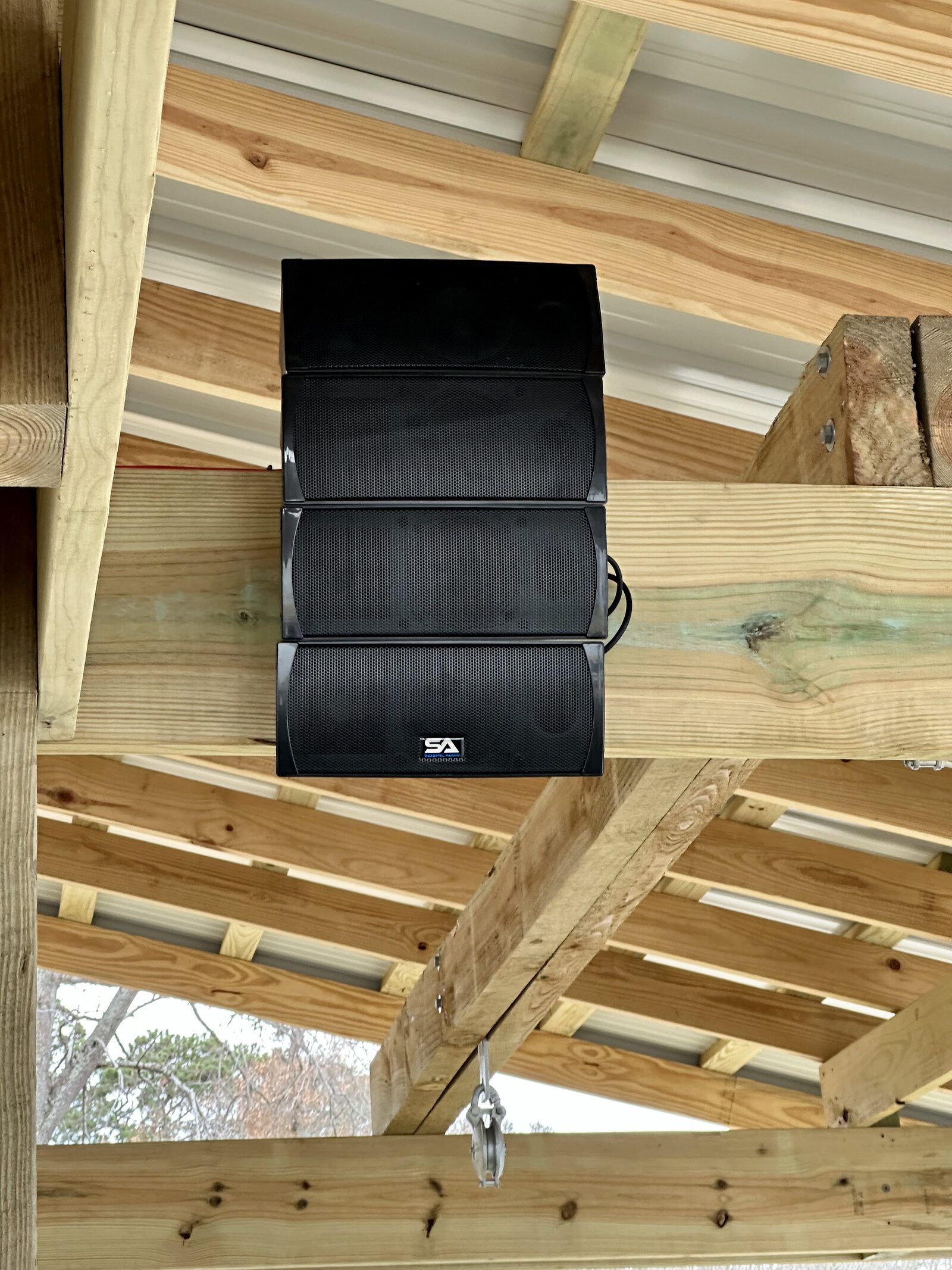 An outdoor speaker mounted to a timber beam under a boathouse roof, wiring run along the framing out of the weather