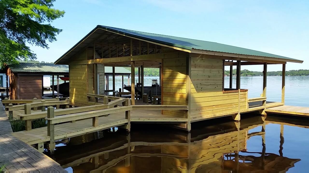 Boathouse with green metal roof and open sides, a boat moored inside, calm water below