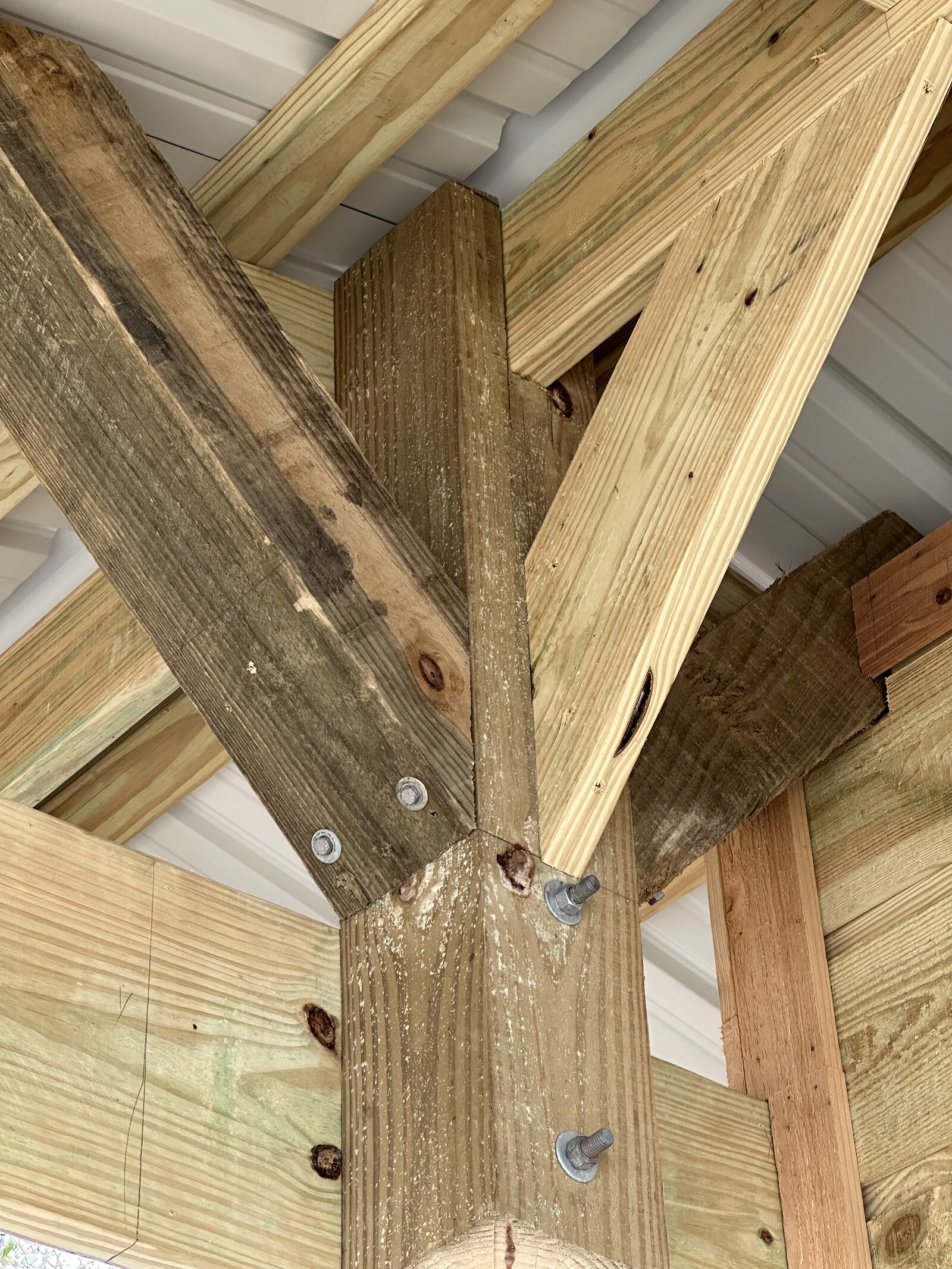 A corner post on a timber boathouse frame with four diagonal knee braces radiating off it in different directions, each through-bolted with galvanized hardware and washers