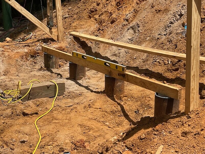 A row of driven steel pipe piles at a bridge abutment after being cut to a common elevation, a timber frame marking the bearing line across the excavation