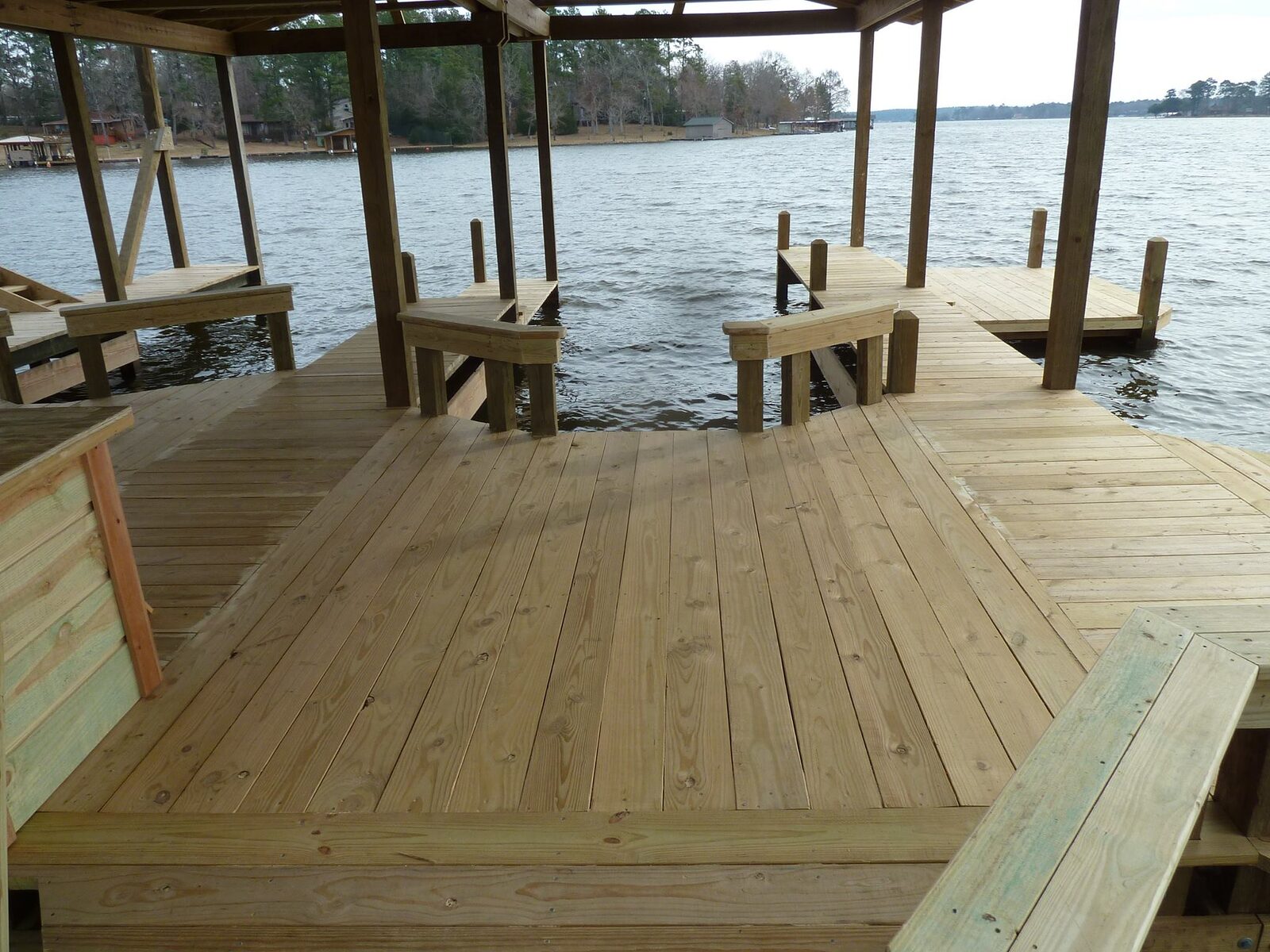Newly laid pale decking under a boathouse roof with integrated bench seating around the perimeter and open lake beyond