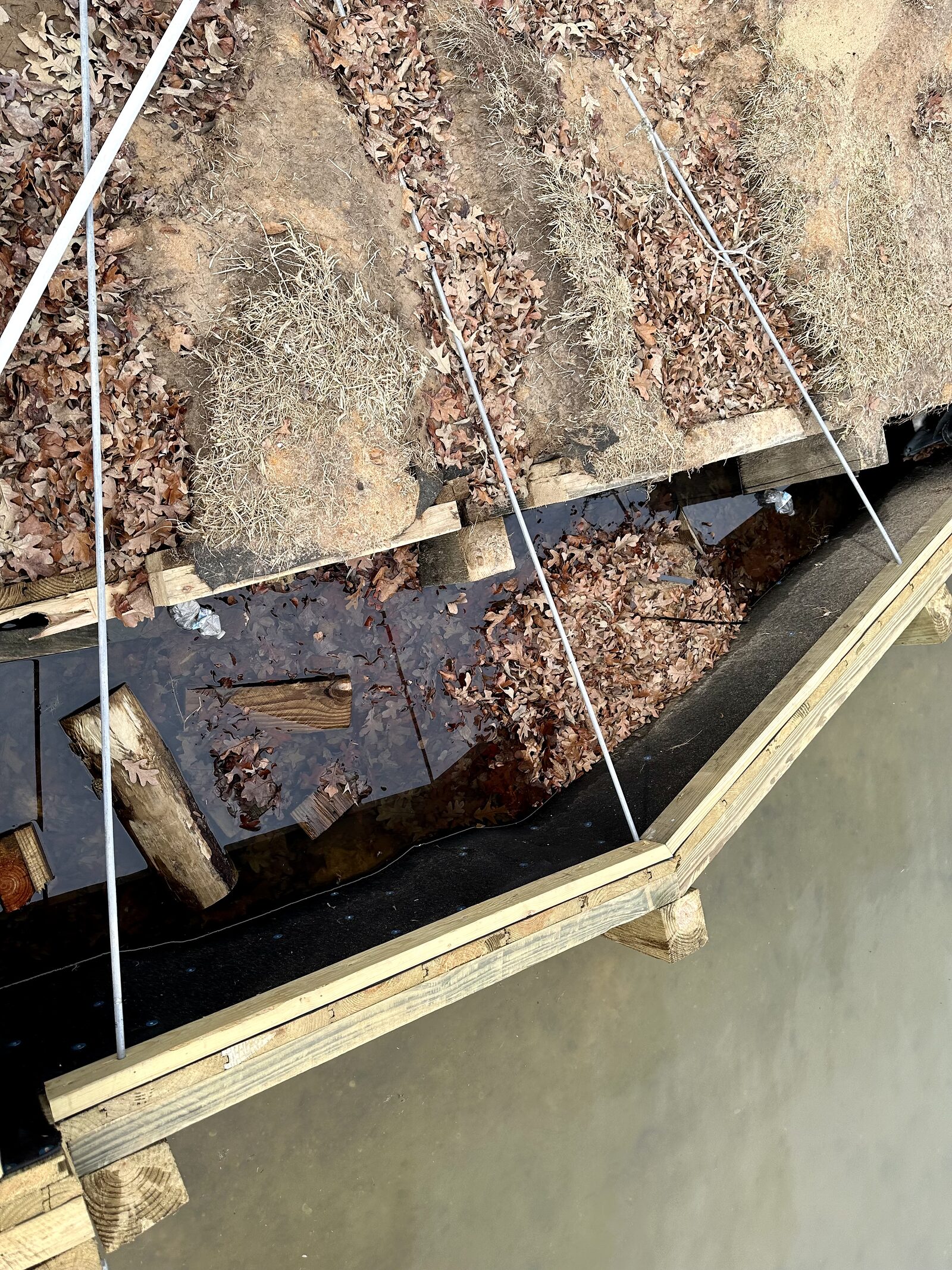 Looking straight down between a new bulkhead and the shore at the old collapsed timber structure lying submerged behind it, with geotextile filter fabric laid and a new timber cap in place