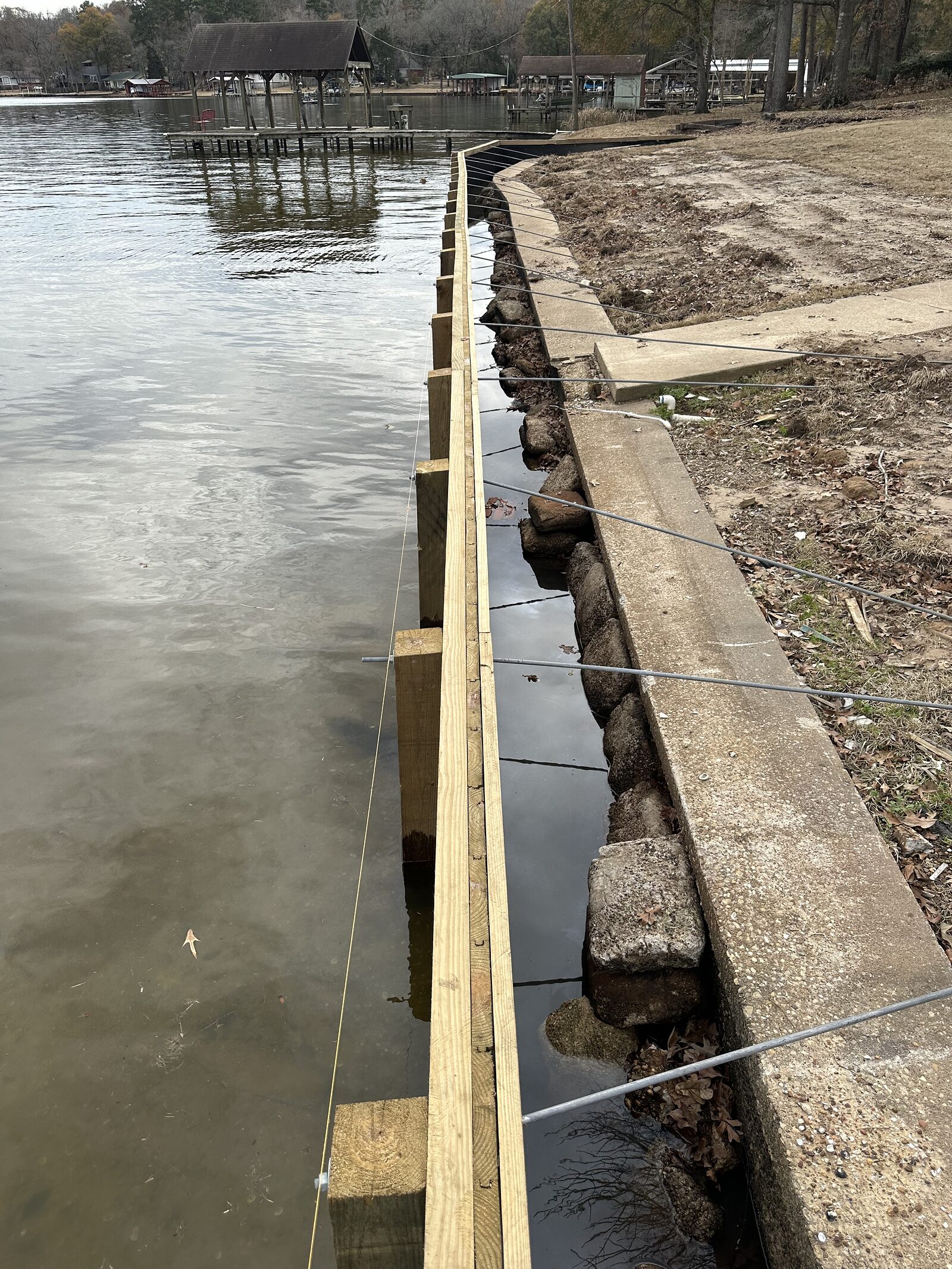New sheet piling with a treated timber wale and cap driven just outboard of a badly failed concrete wall, steel tie-back rods running back over it and dumped riprap rock between