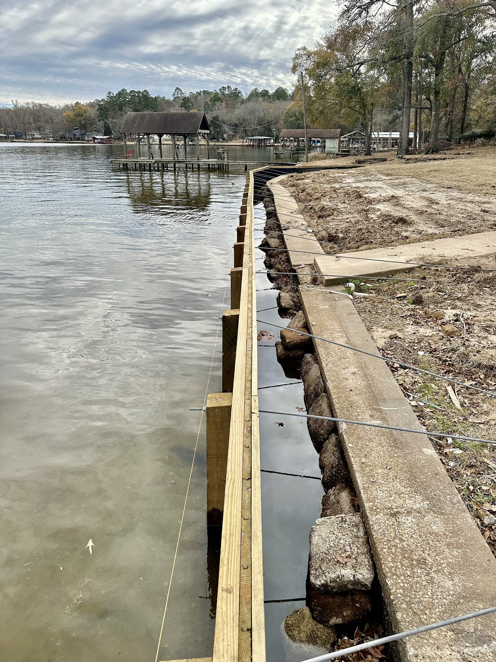 Steel tie-back rods at regular spacing across a bulkhead run, running back from the wall toward the shore with open water beyond