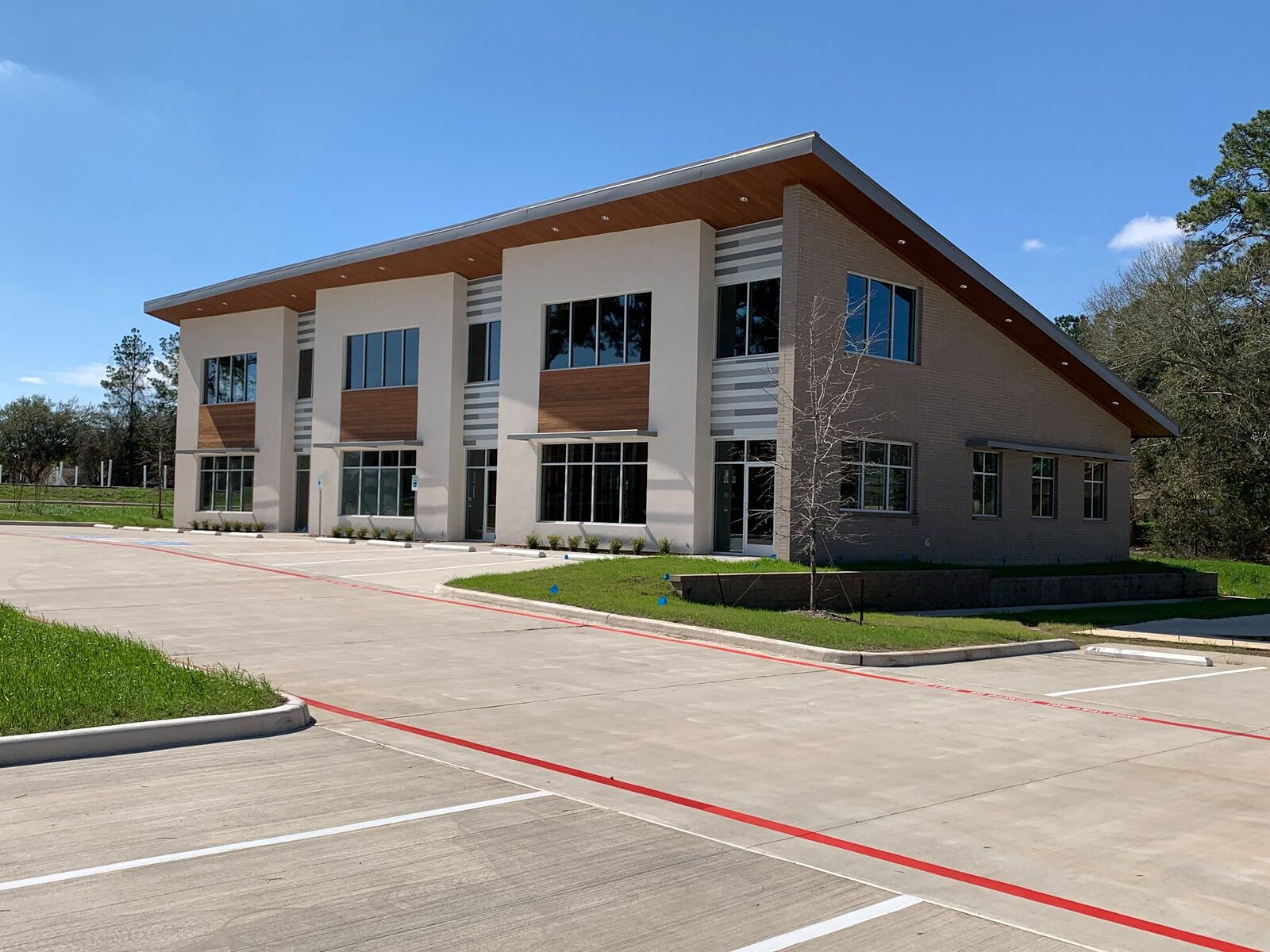 Completed two-story commercial office building with a sloped metal roof, brick and stucco facade, and new concrete parking lot