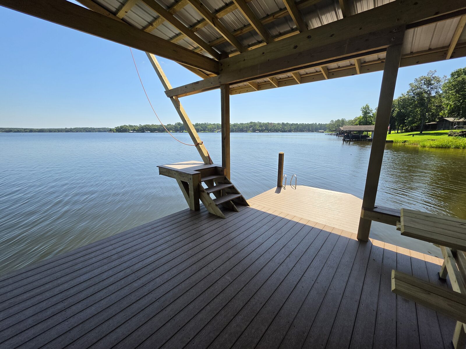 A finished composite boathouse deck in dark brown boards, stair and bench in frame, open lake beyond the slip