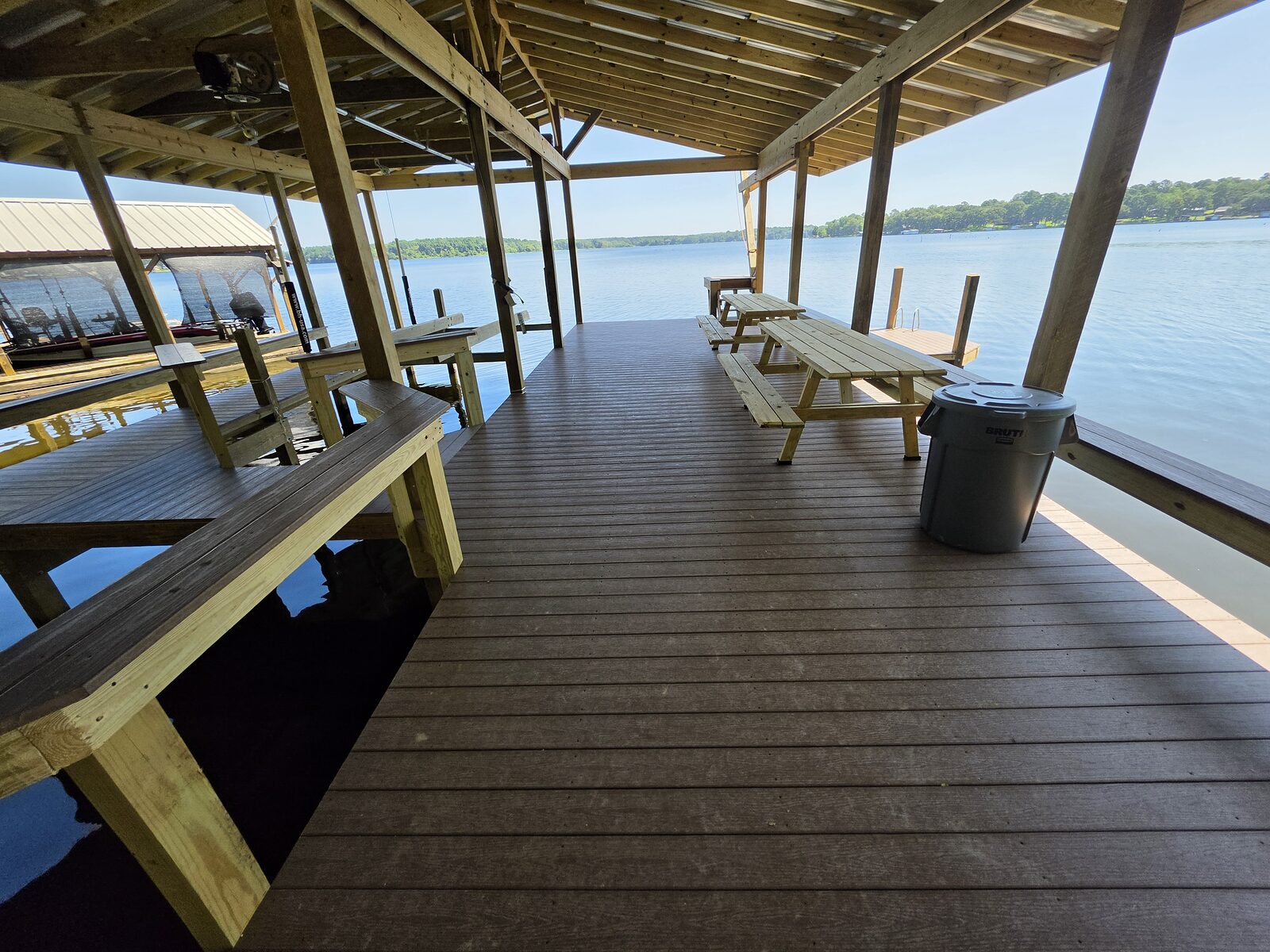 A composite boathouse deck with fixed bench seating and a picnic table under the roof, looking out over open water