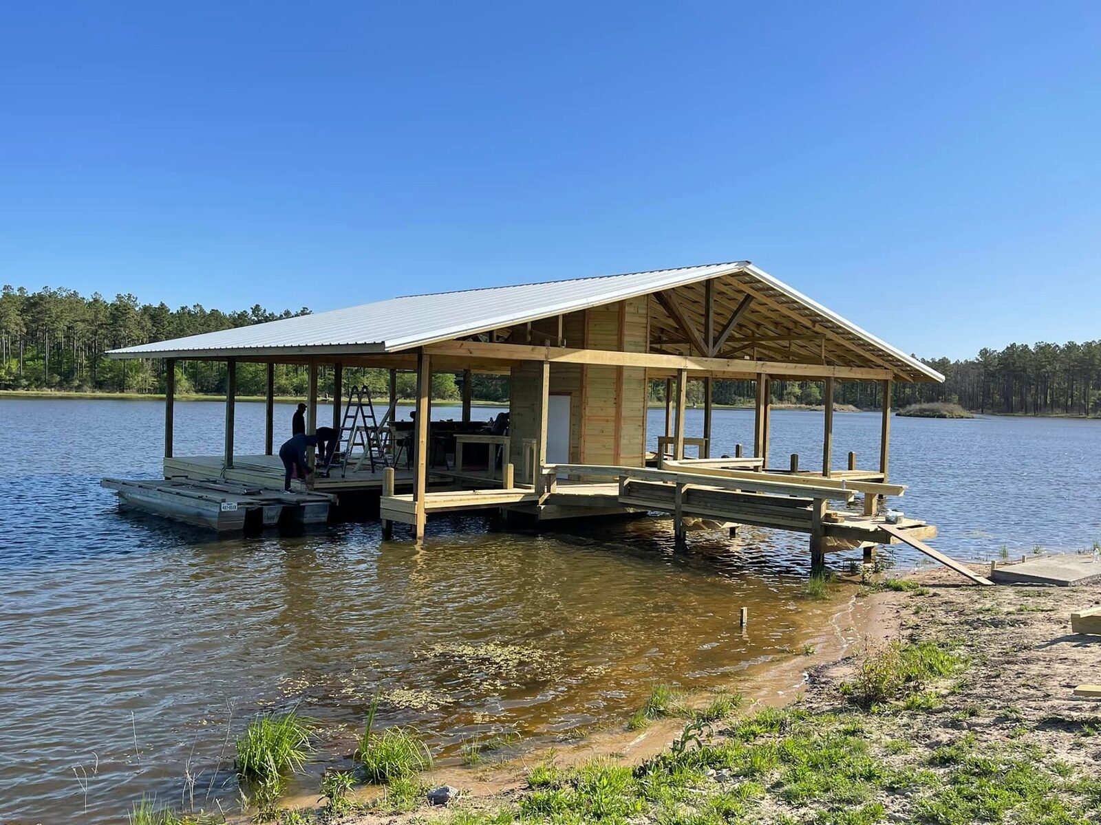 Newly built covered boathouse with a metal roof and timber decking over a calm lake
