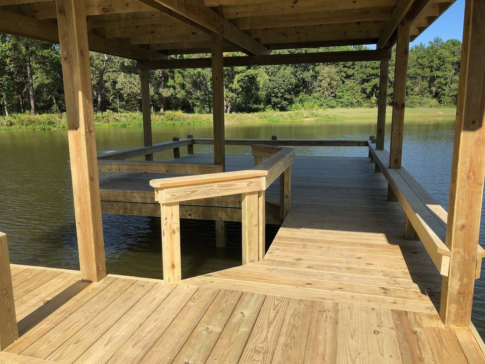 Covered pier head over a private pond with bench railing and a kayak slip cut into the deck