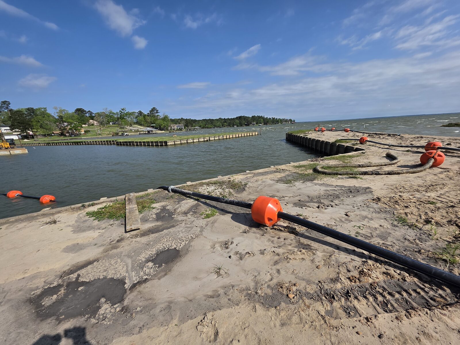 A dredge discharge line on orange floats running along a finished bulkhead and out across the lake to a barge working offshore
