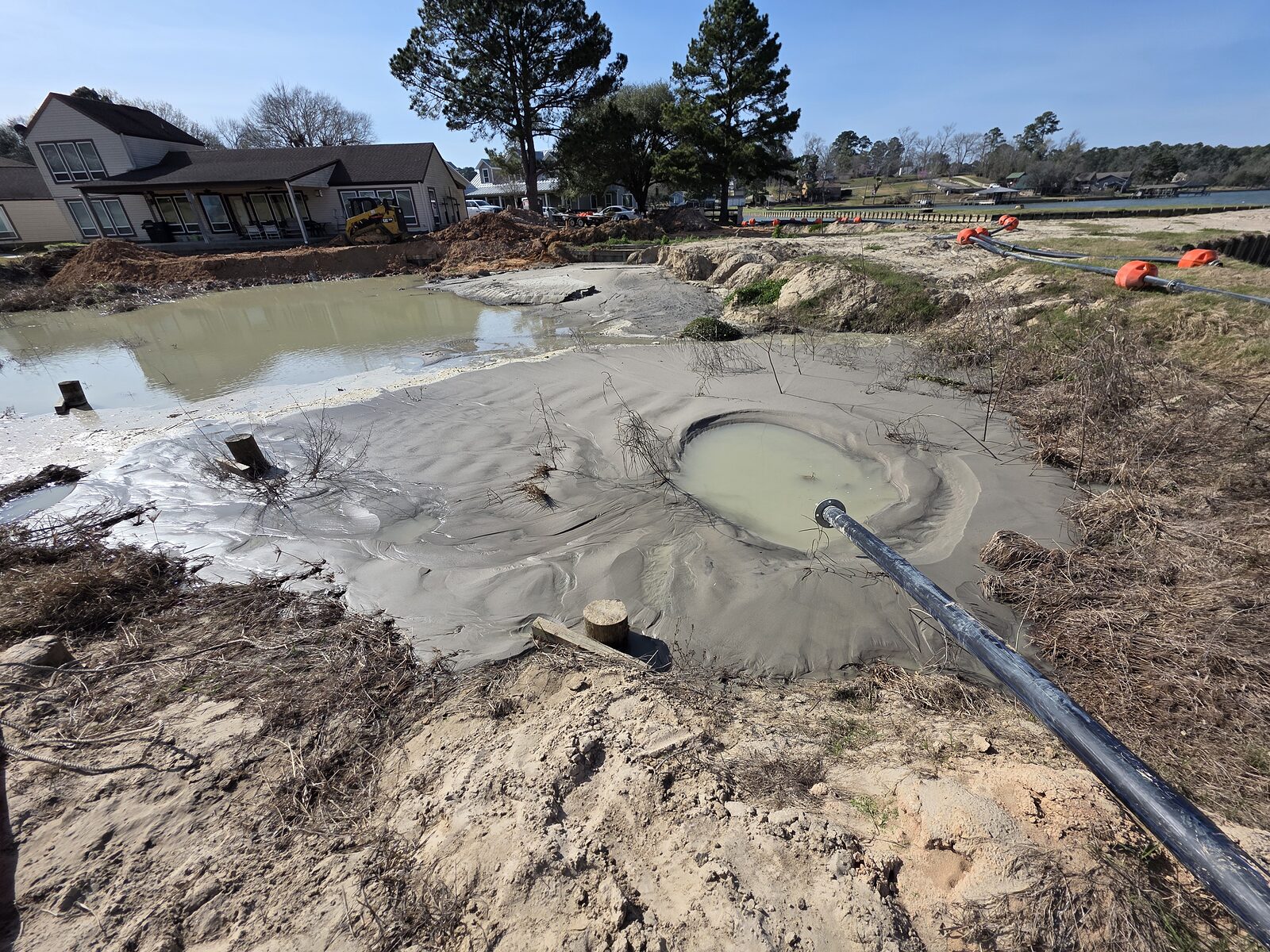 A settling pond behind the shoreline with dredged slurry discharging into it, the water clearing as the solids drop out