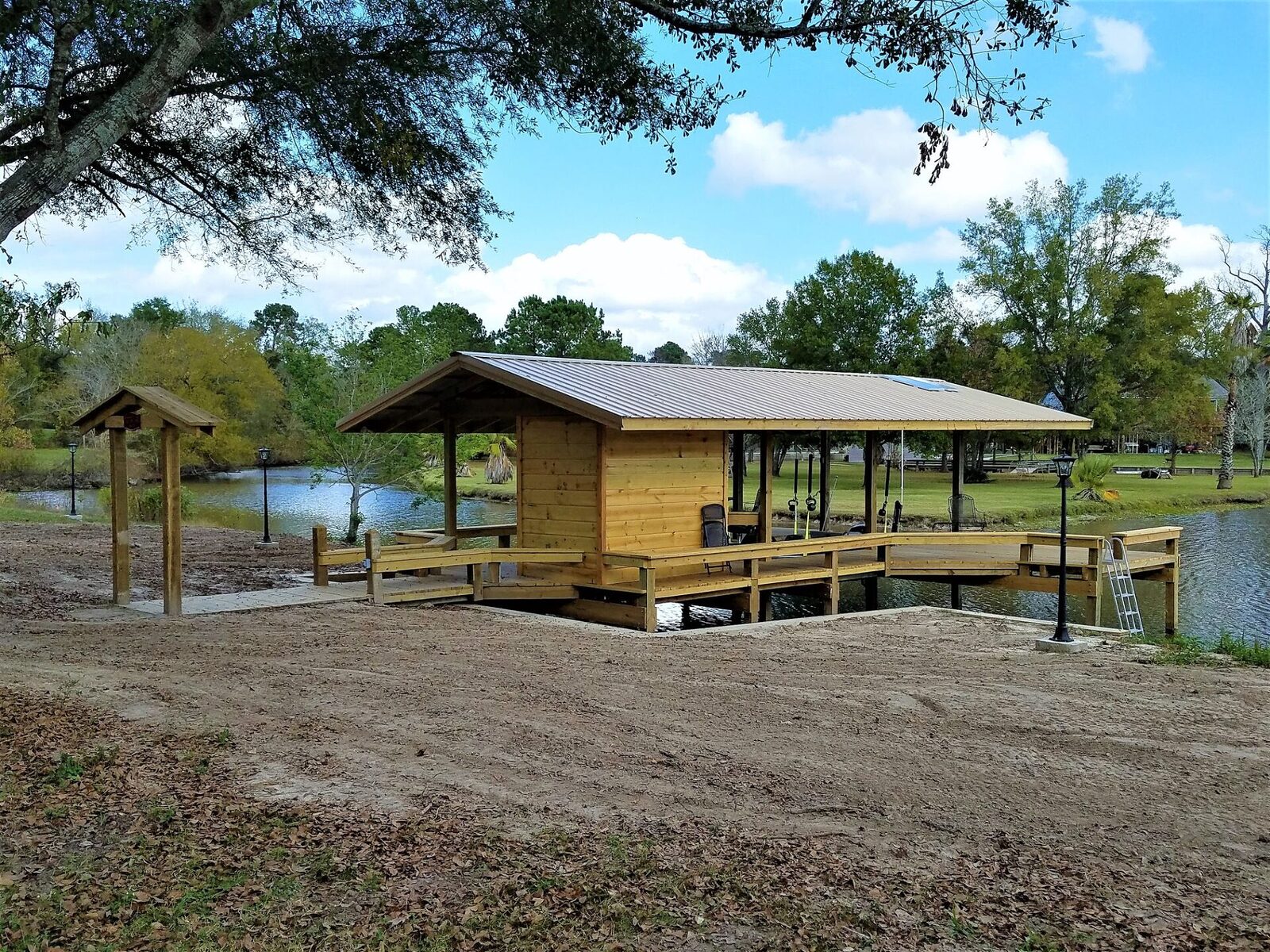 Completed wood boathouse with metal roof, covered slip and railed walkway beside a calm pond