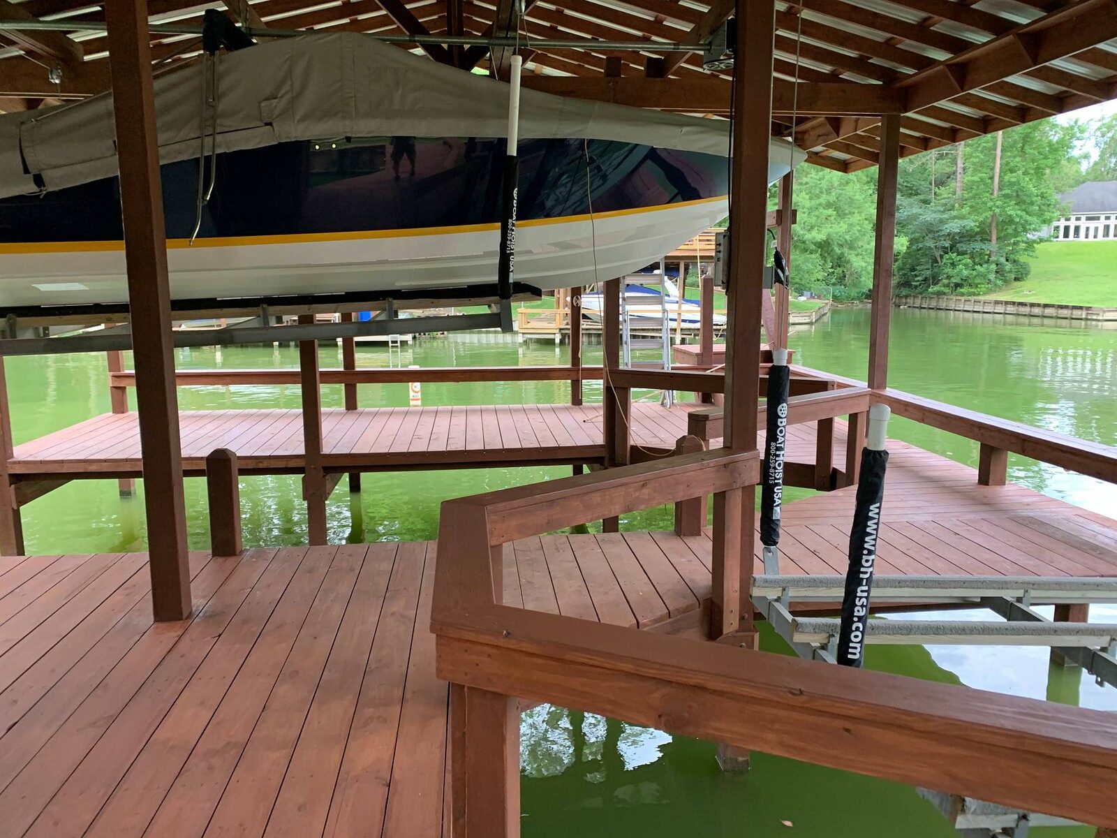 Boat raised on a lift inside a finished covered boathouse with stained wood decking
