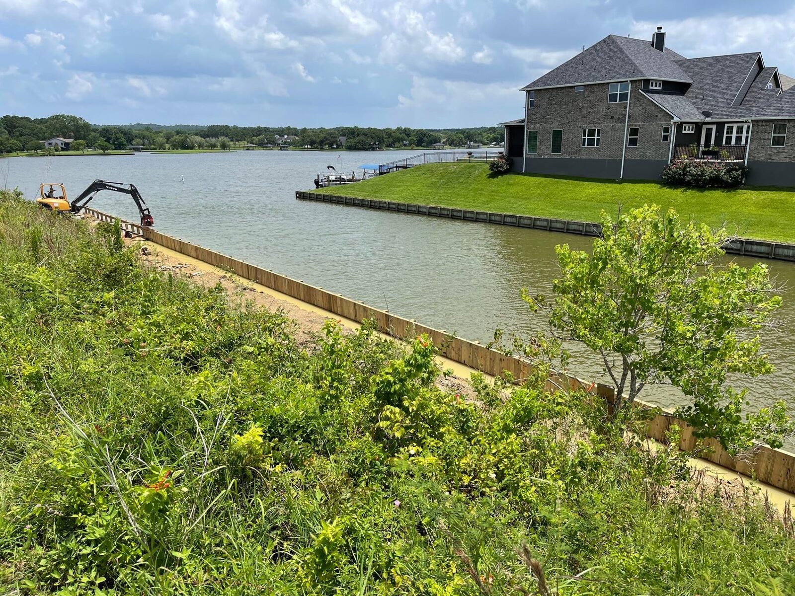 Completed bulkhead holding a green lawn in front of a large lakefront home, with a newly built timber bulkhead running along the near shoreline