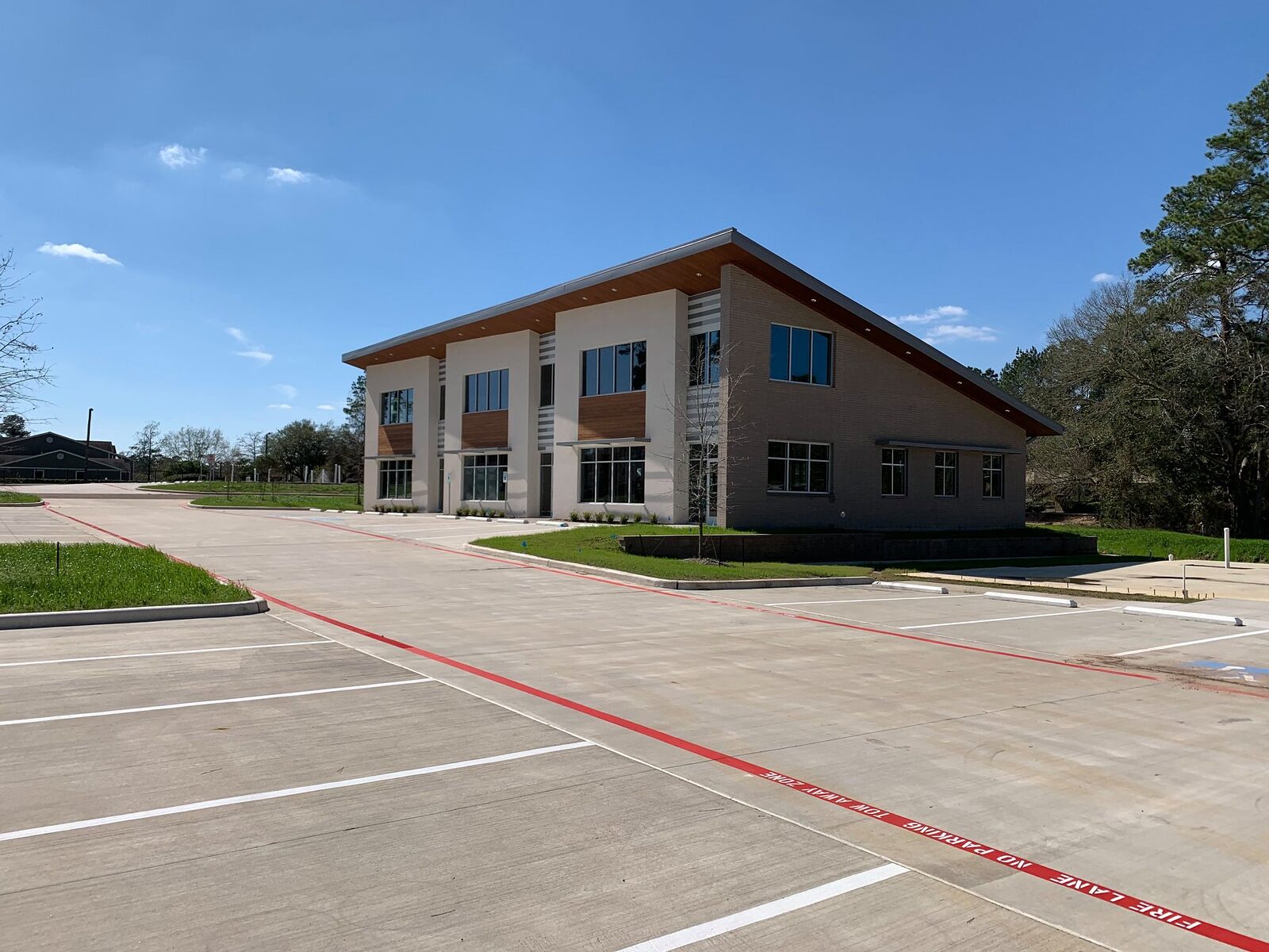 Wide view of newly poured and striped concrete parking lot with a red fire lane in front of a finished commercial office building