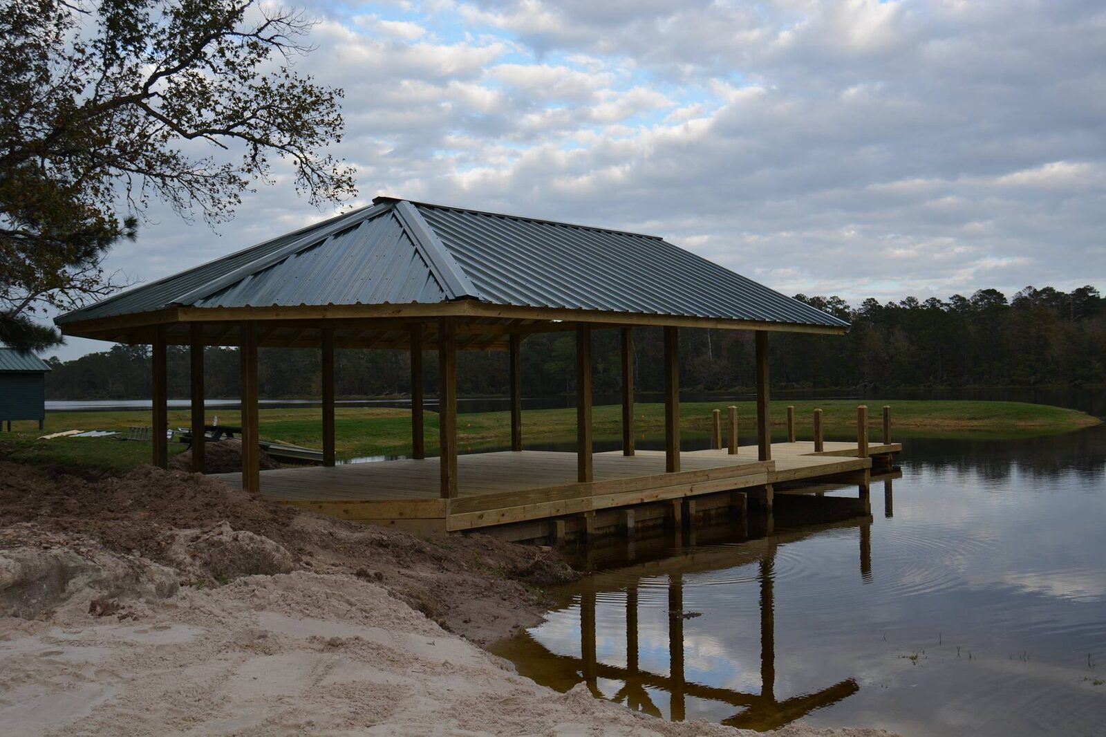 Large hip-roof shelter on timber piles with a wooden walkway extending out over the water at dusk