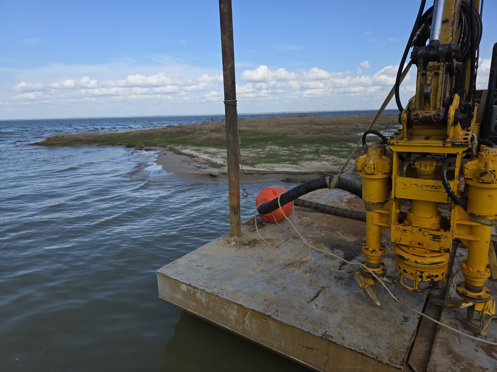 A hydraulic dredge pump mounted on a barge deck, hose and floats rigged alongside, working on open water
