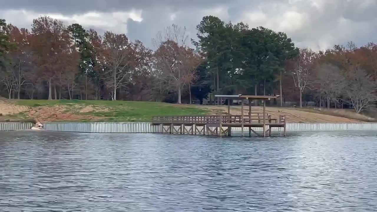 Completed galvanized steel sheet-pile seawall running along a lawn, with a timber pier