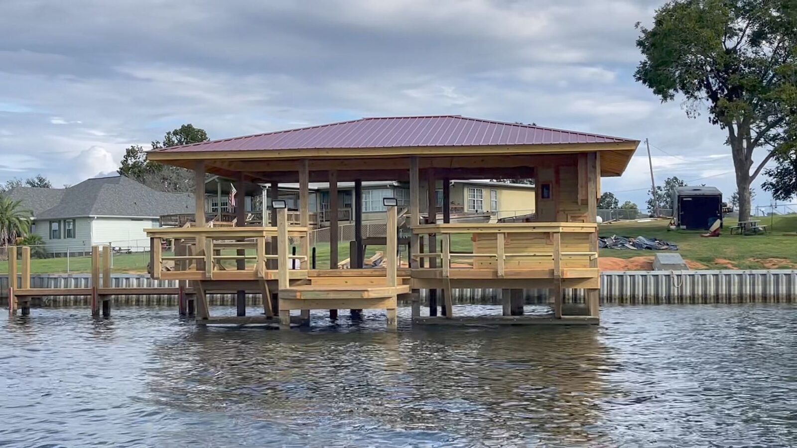 Finished boathouse with a red metal roof standing over the water next to a new steel sheet-pile bulkhead along the shoreline at Lake Nacogdoches