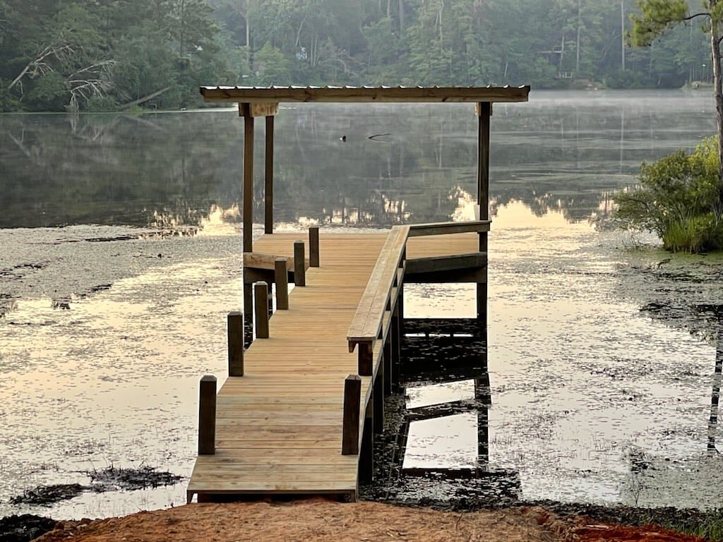Covered pier with bench railings built by Shoretech on Lake Livingston, extending over still water at dawn