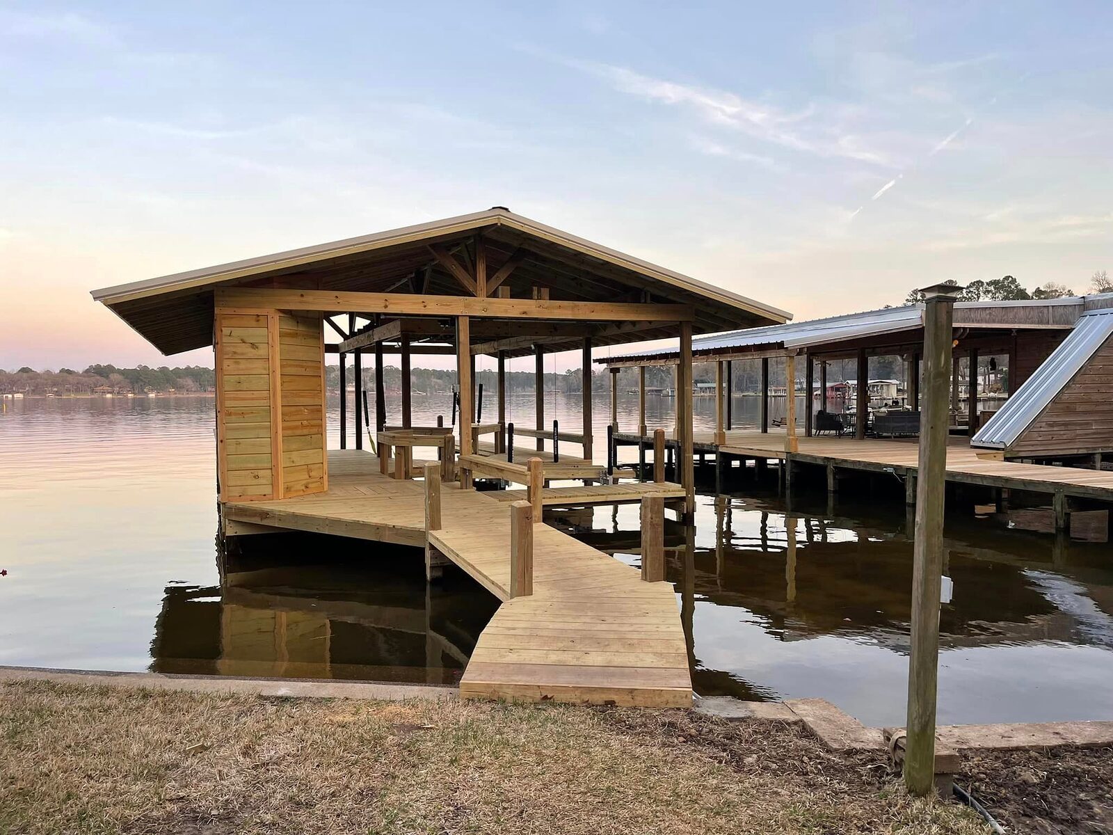Covered double-slip boathouse and wood walkway built by Shoretech over Houston County Lake at dusk
