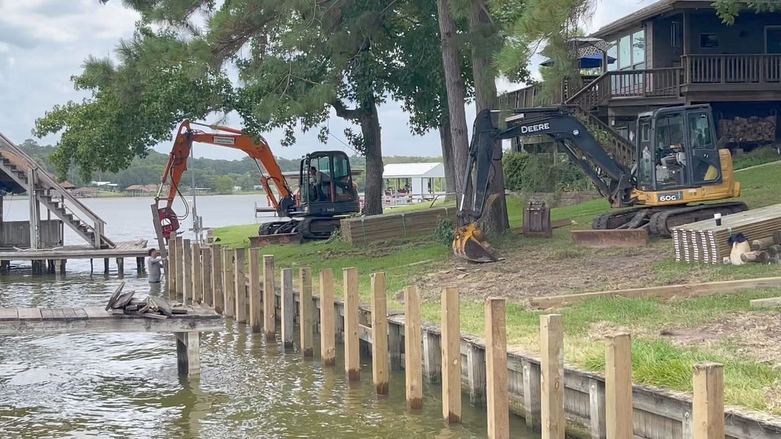 New timber bulkhead and row of pilings along a lakefront yard, excavators working on the bank