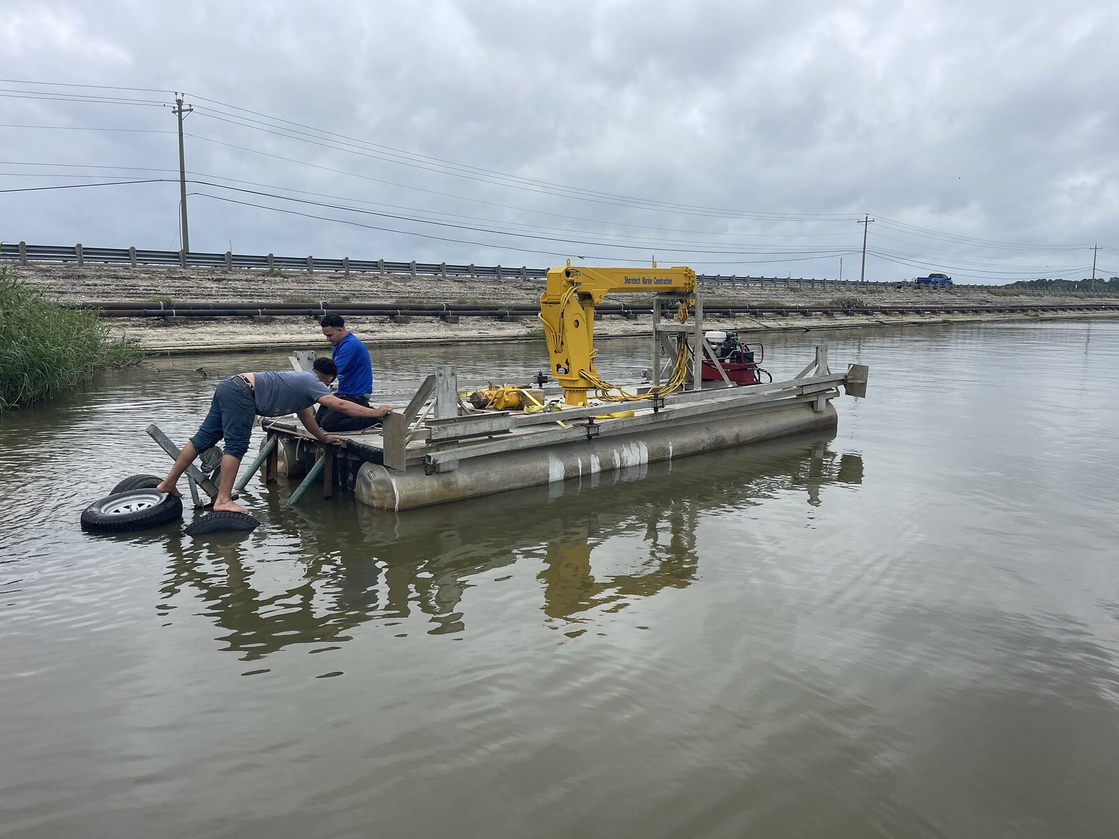 Shoretech crew working on the dredge barge in a shallow channel, boom arm raised over the deck