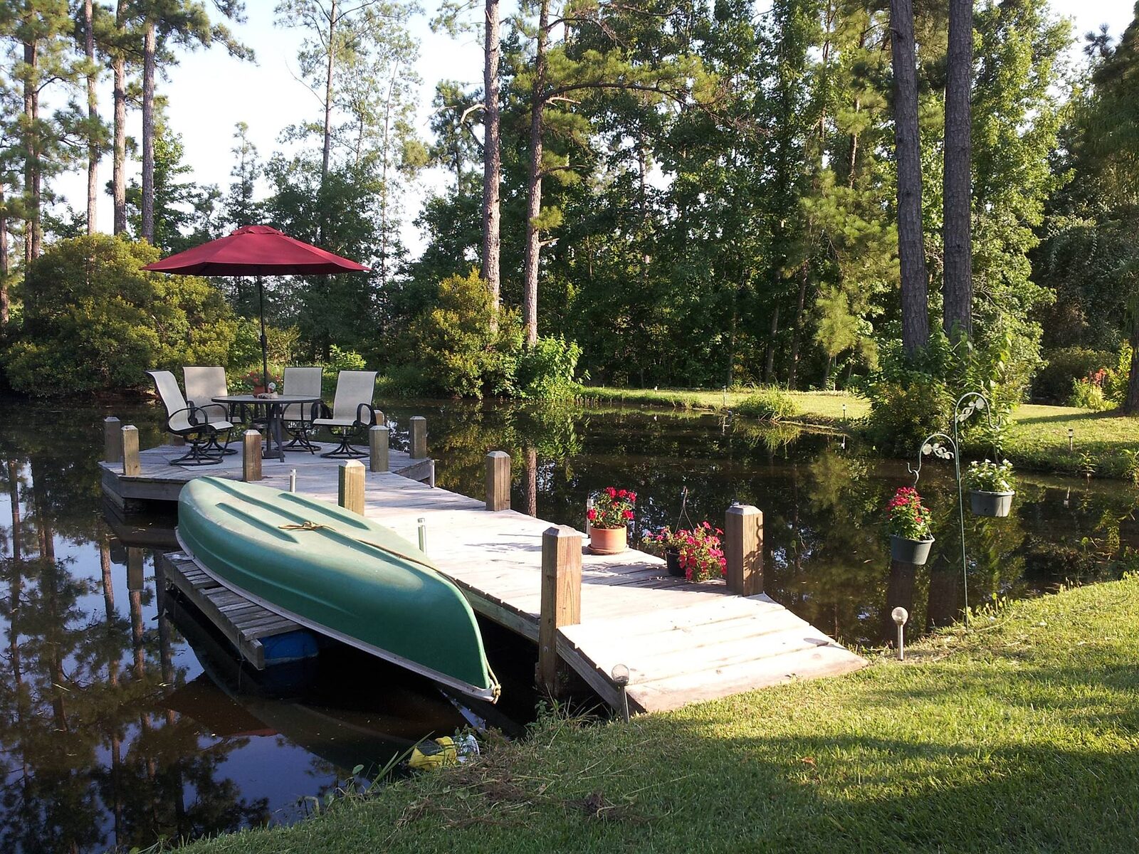 Wooden pond dock with patio table and umbrella, and a green canoe stored on the lower decking