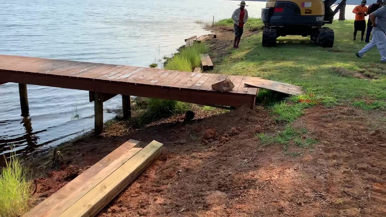 Timber pier extending over a lake while a crew and excavator prepare the eroded shoreline for a new bulkhead