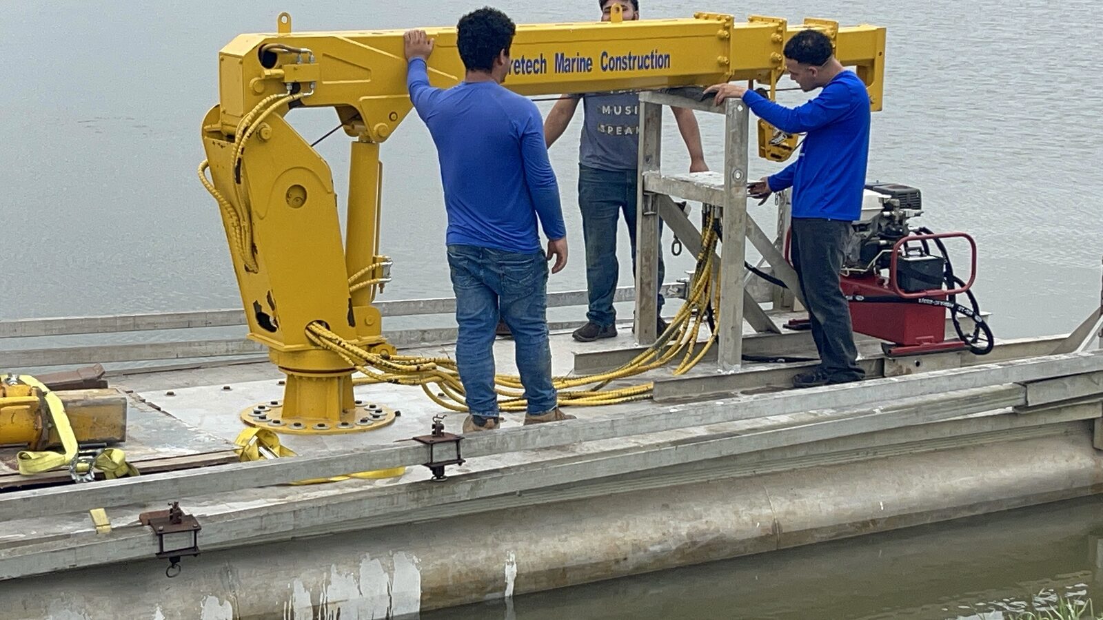 Shoretech crew fitting the yellow dredge boom and its power pack to the barge deck at the water's edge