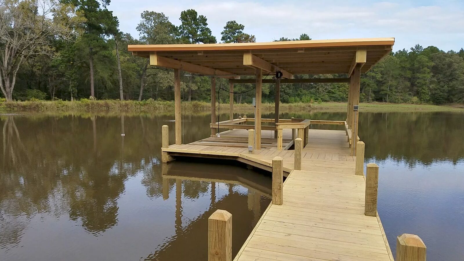 Covered single-slip boathouse and approach walkway reflected in a still private pond