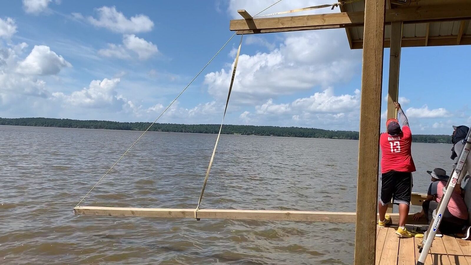 A Shoretech crew member steadying a long timber beam slung on straps as it swings out over open water into position
